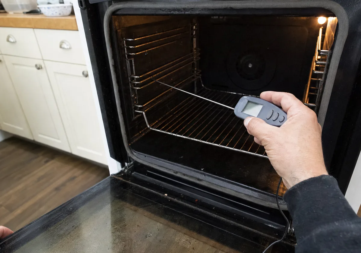A thermometer readout held at the mouth of an open oven, probe wire over the rack