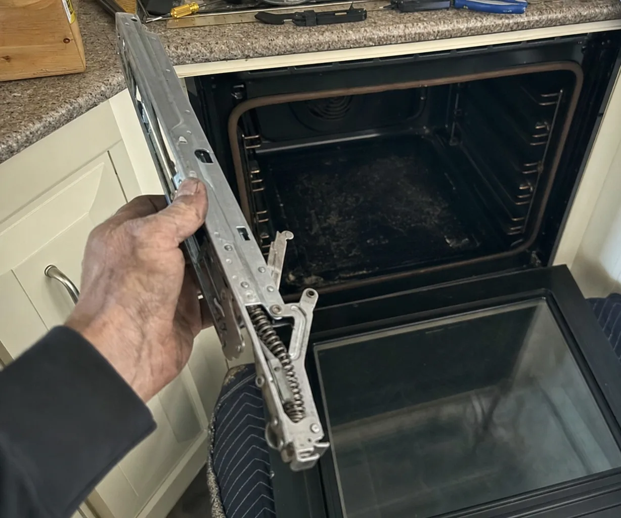 The spring hinge of a heavy oven door, removed and held up for inspection