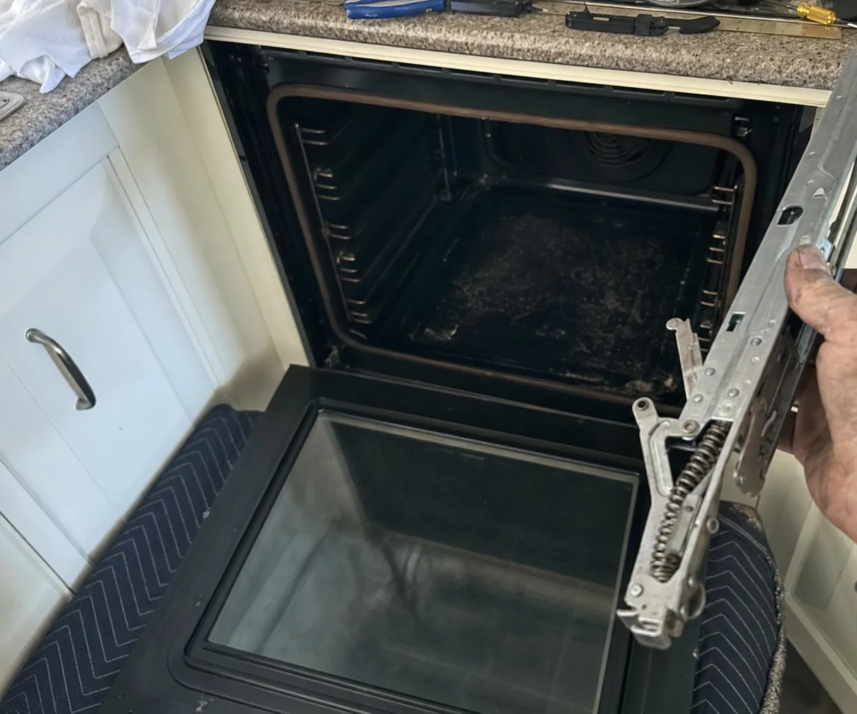 An oven door lifted off its hinges and set down on a padded chair beside the appliance